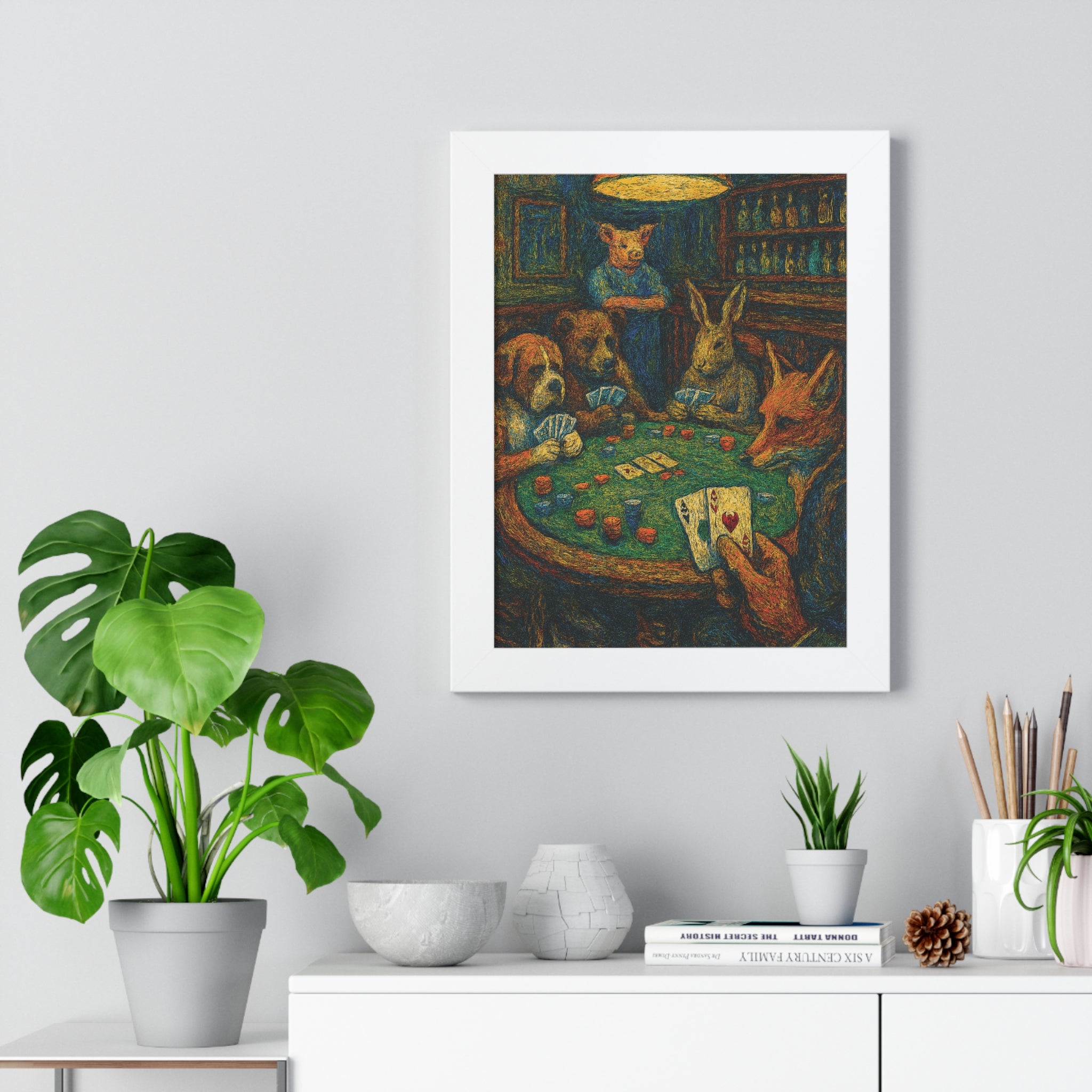 Framed artwork of animals playing cards on a wall above a white cabinet with plants.