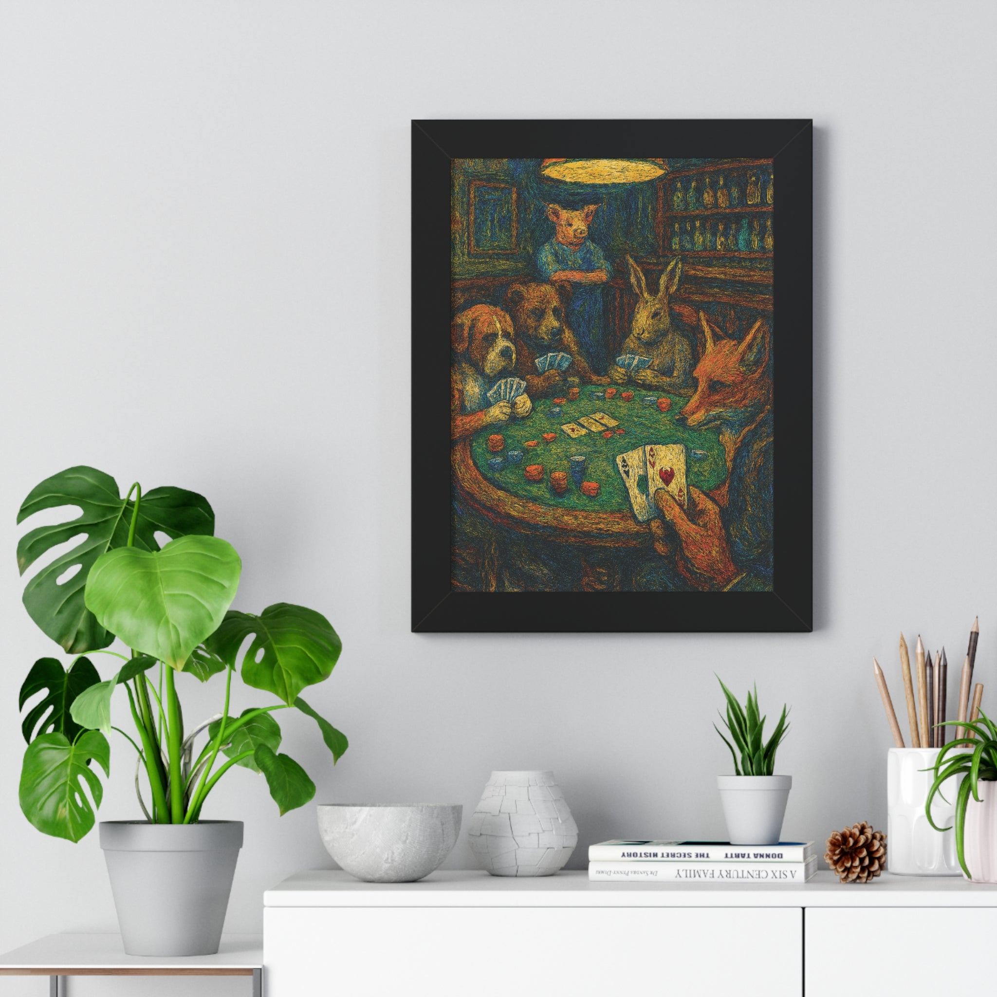 Framed artwork of animals playing cards on a wall above a white cabinet with plants.