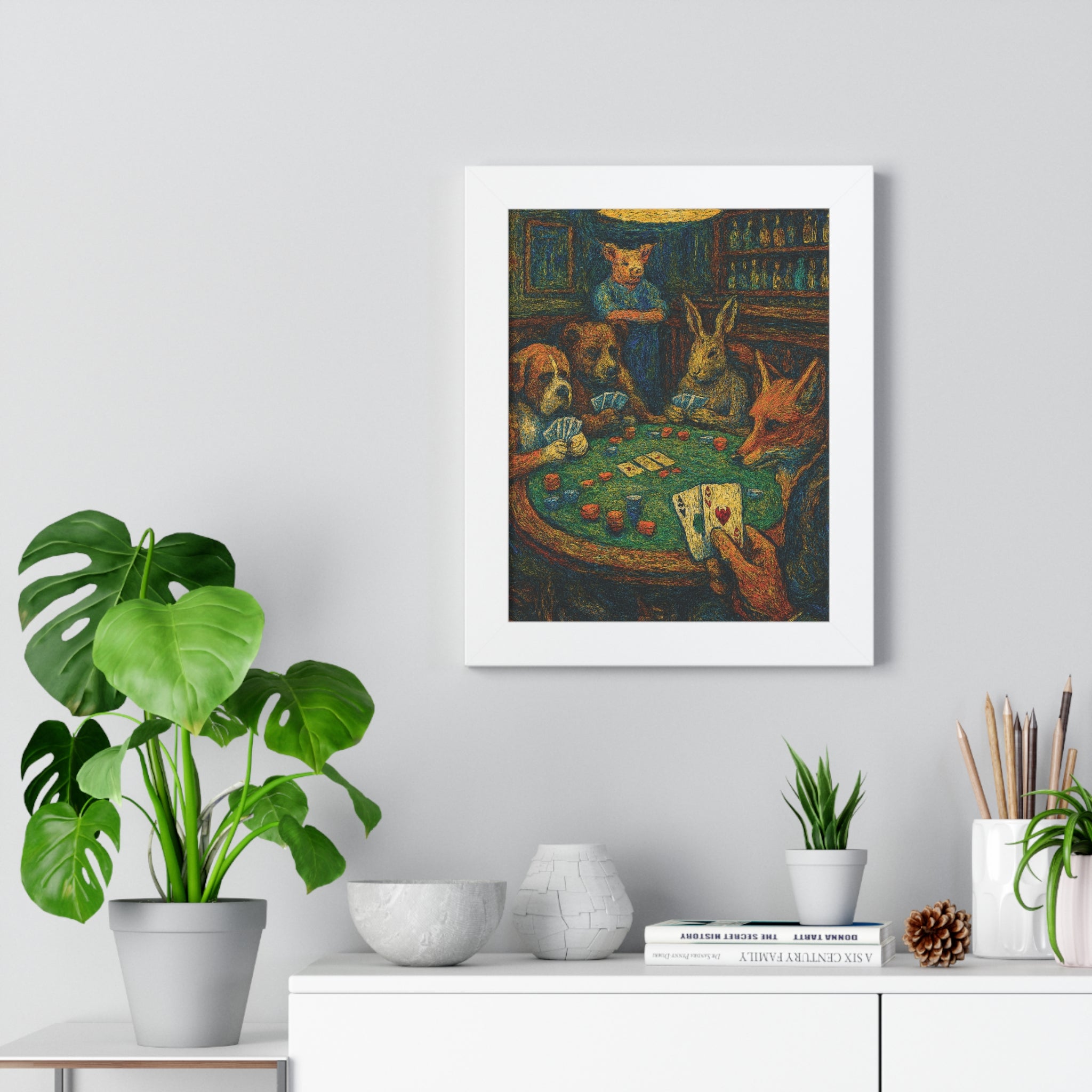 Framed artwork of animals playing cards on a wall above a white cabinet with plants and decor.